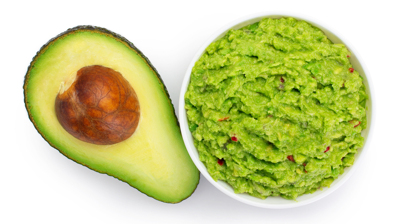 Tazón de guacamole fresco junto a una mitad de aguacate con el hueso.